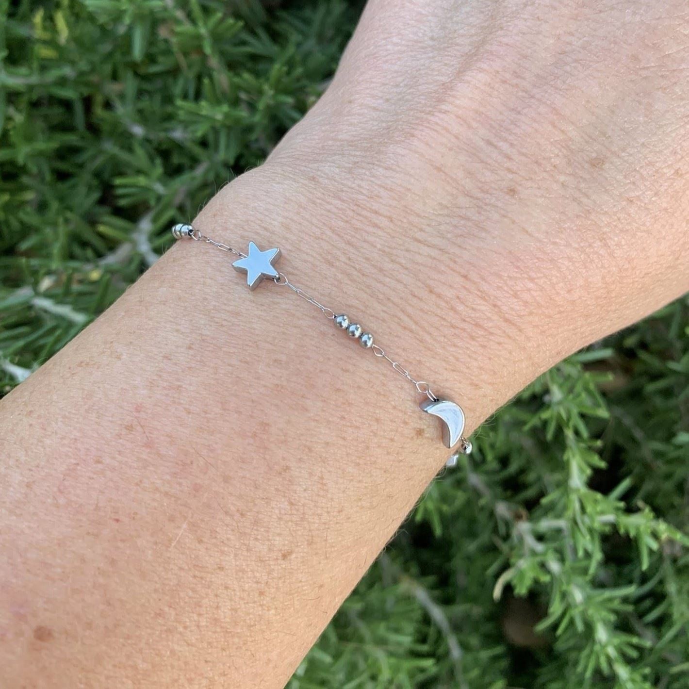 Bracelet with star and moon charms on a wrist against a green leafy background